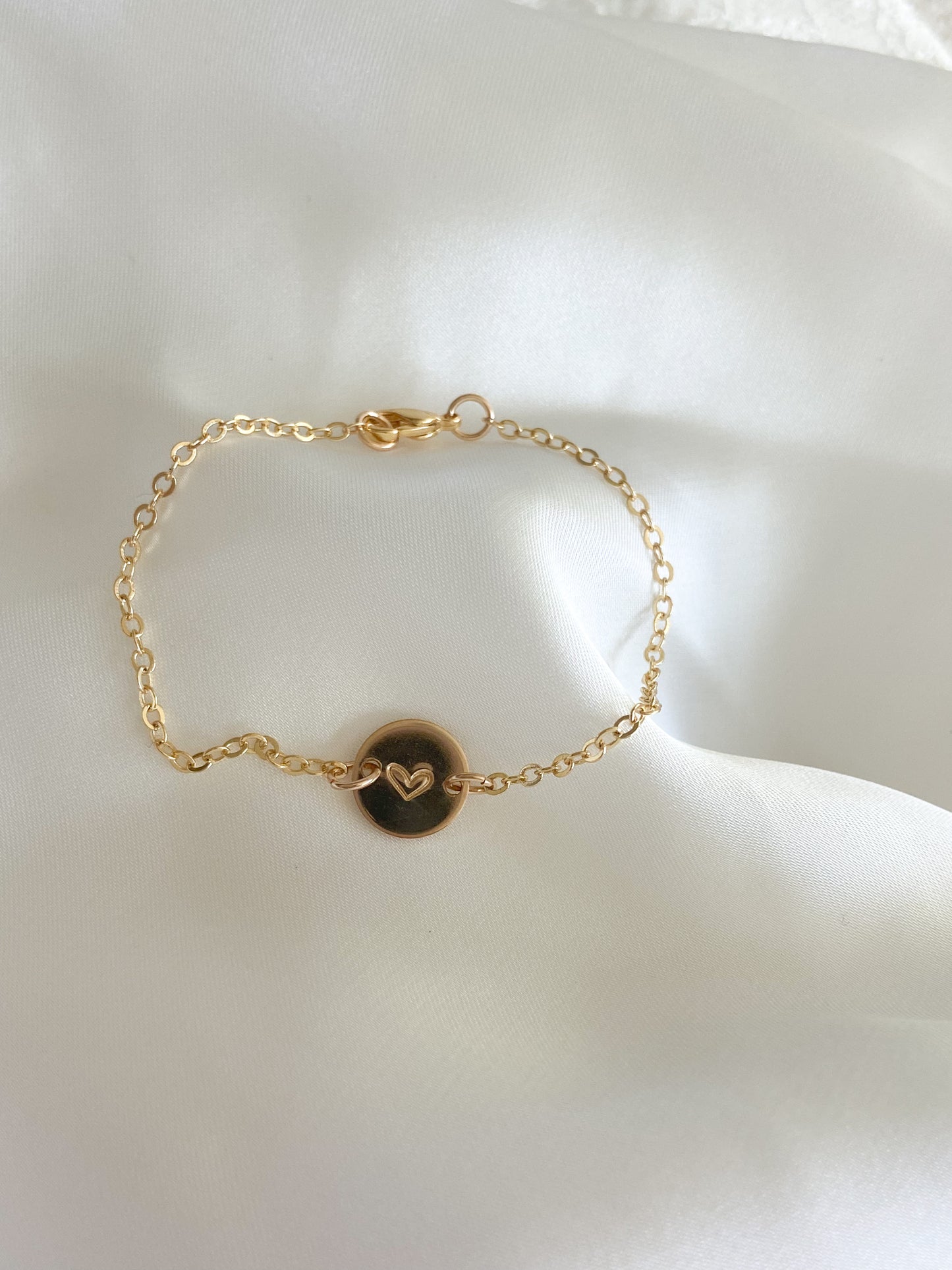 A gold necklace with a heart stamped on it, laying on a white background