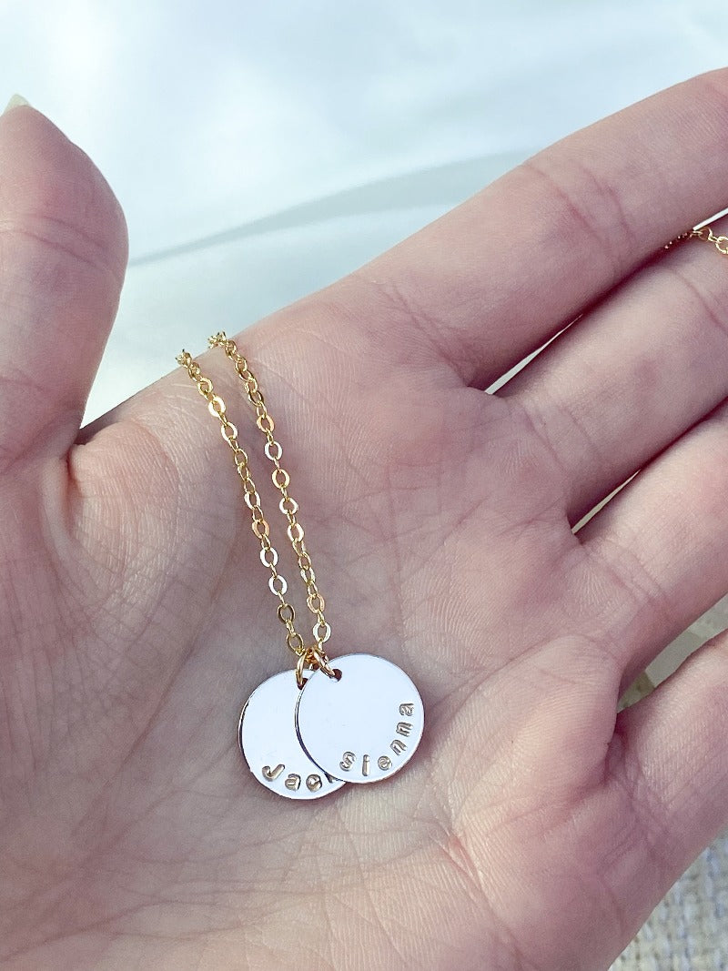 Hand holding a gold necklace with two discs, one that says Sienna and one that says Jack.