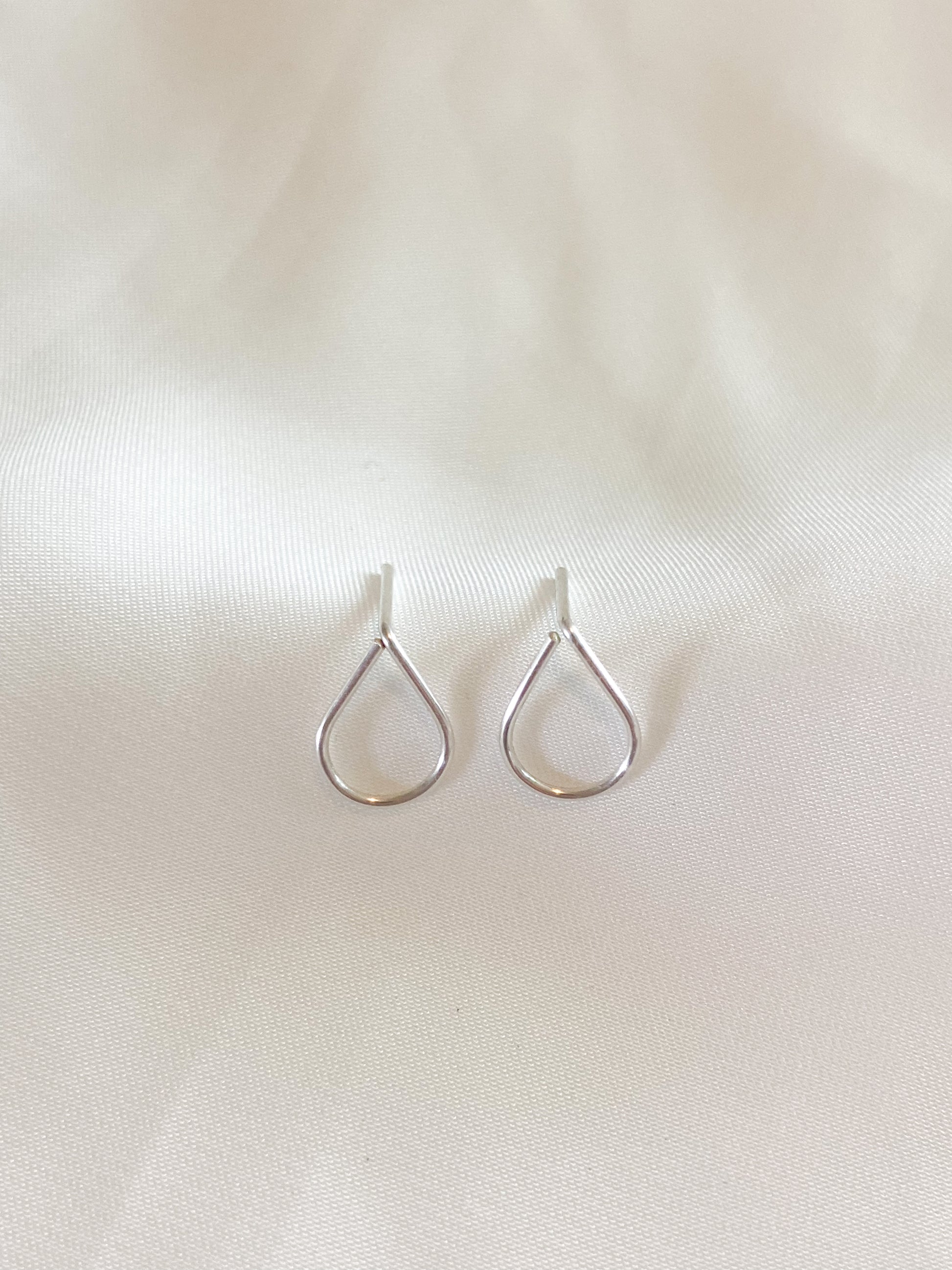 Sterling Silver wire teardrop shaped earring studs on white background.